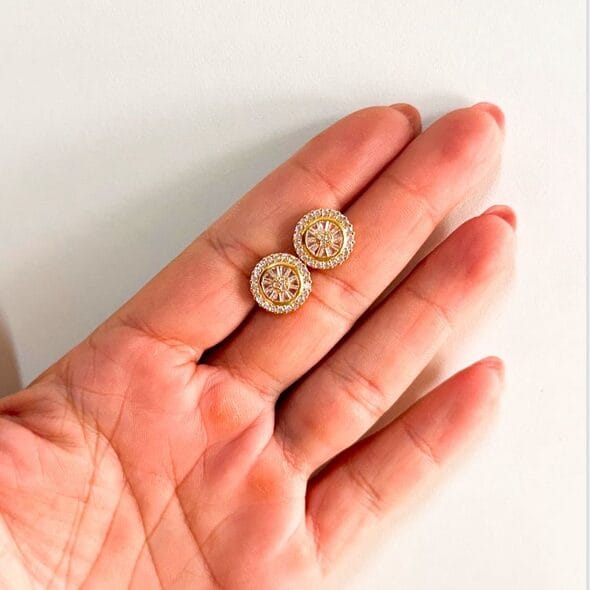 Pair of Round Zirconia Stud Earrings with 18K gold-plated finish and sparkling zirconia halo, displayed on an open hand against a white background.
