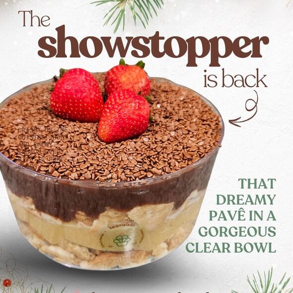 Close-up of Karamelado’s Double Brigadeiro Pavê in a transparent bowl, highlighting the layers of creamy white brigadeiro, rich chocolate brigadeiro, and biscuit pieces. The top is covered with chocolate sprinkles and garnished with fresh strawberries, creating a festive and indulgent look.