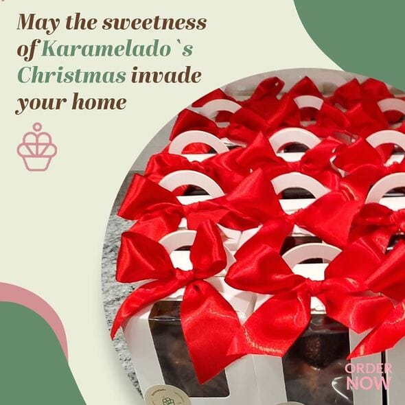 Mini Brazilian-style Brigadeiro panettone from Karamelado, presented in an elegant white box with a clear window and topped with a large red satin bow. The panettone is decorated with a glossy chocolate glaze and topped with brigadeiro truffles, creating a festive and indulgent look. The box is placed on a granite countertop, perfect for holiday gifting