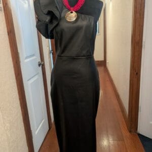 Black maxi dress made of nappa‑style faux leather displayed on a mannequin, featuring a one‑shoulder ruffle detail and sleek silhouette, designed for elegant resort evenings by Fashion Brasil Sun and Sea.
