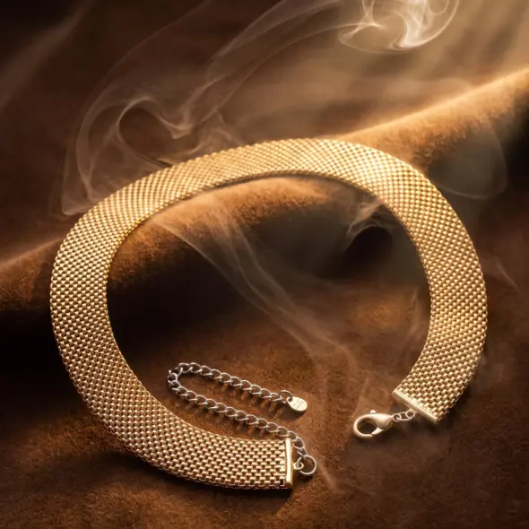 Wide gold-tone mesh collar necklace with a flexible woven design and adjustable chain extension, displayed on a luxurious warm background, representing modern elegance and timeless sophistication by Madu Joia Rara.