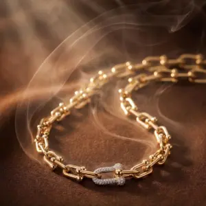 Gold-tone statement link necklace featuring elongated polished links and a sparkling zirconia pavé clasp centerpiece, displayed on a luxurious textured background, symbolizing elegance, strength, and timeless sophistication by Madu Joia Rara.