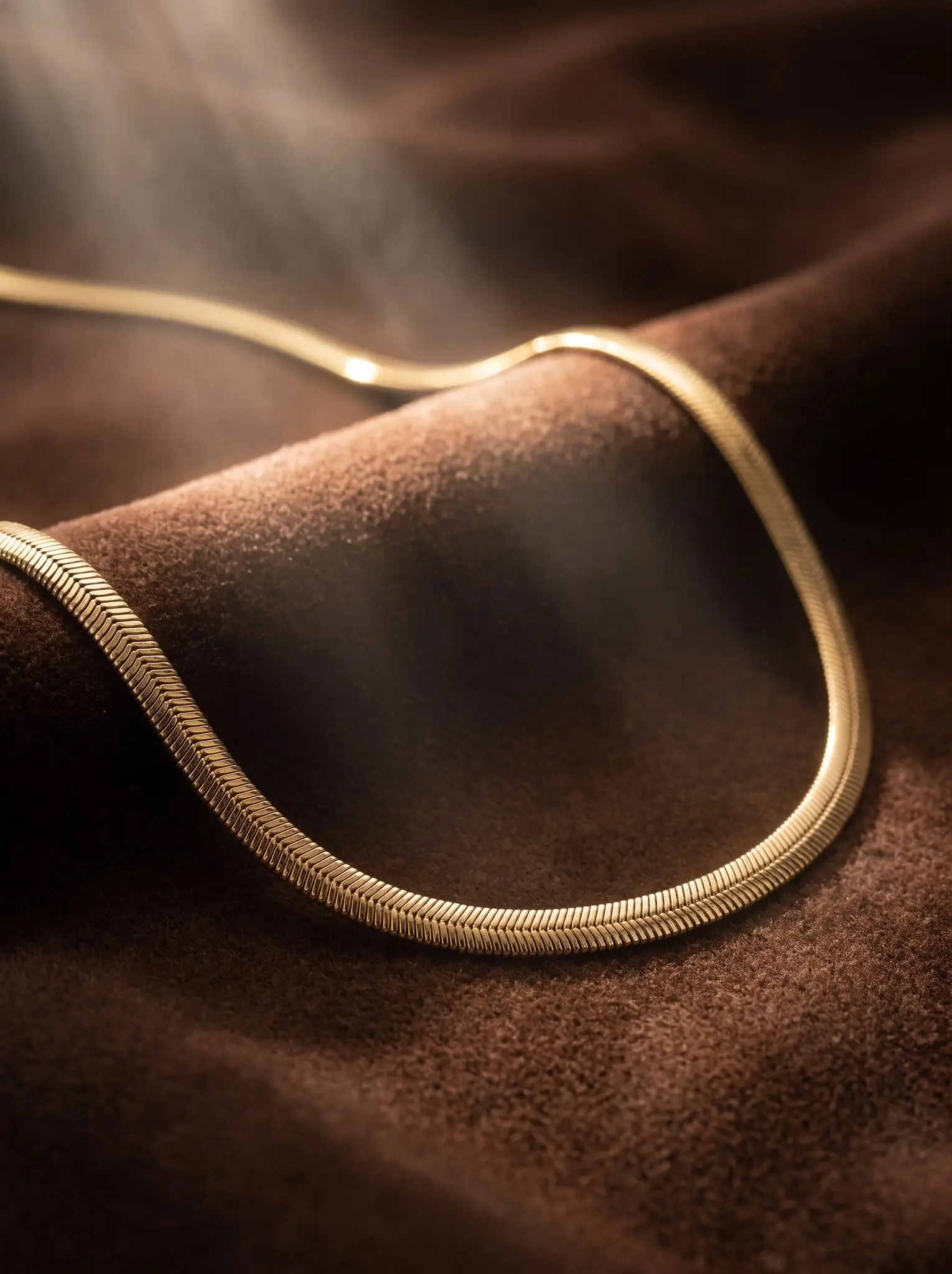 golden serenity herringbone necklace madu joia rara | Golden Serenity Herringbone Necklace – Madu Joia Rara Elegant gold-tone herringbone necklace with a smooth flat design and luminous finish, displayed on a soft brown velvet surface, showcasing timeless sophistication by Madu Joia Rara.